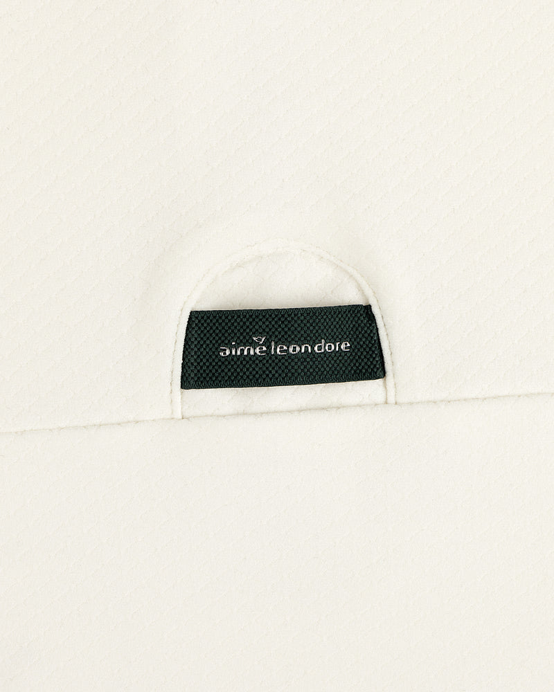 A close-up of a black Aimé Leon Dore label sewn onto the off-white ALD Golf Quarter Zip Pullover’s textured fabric.