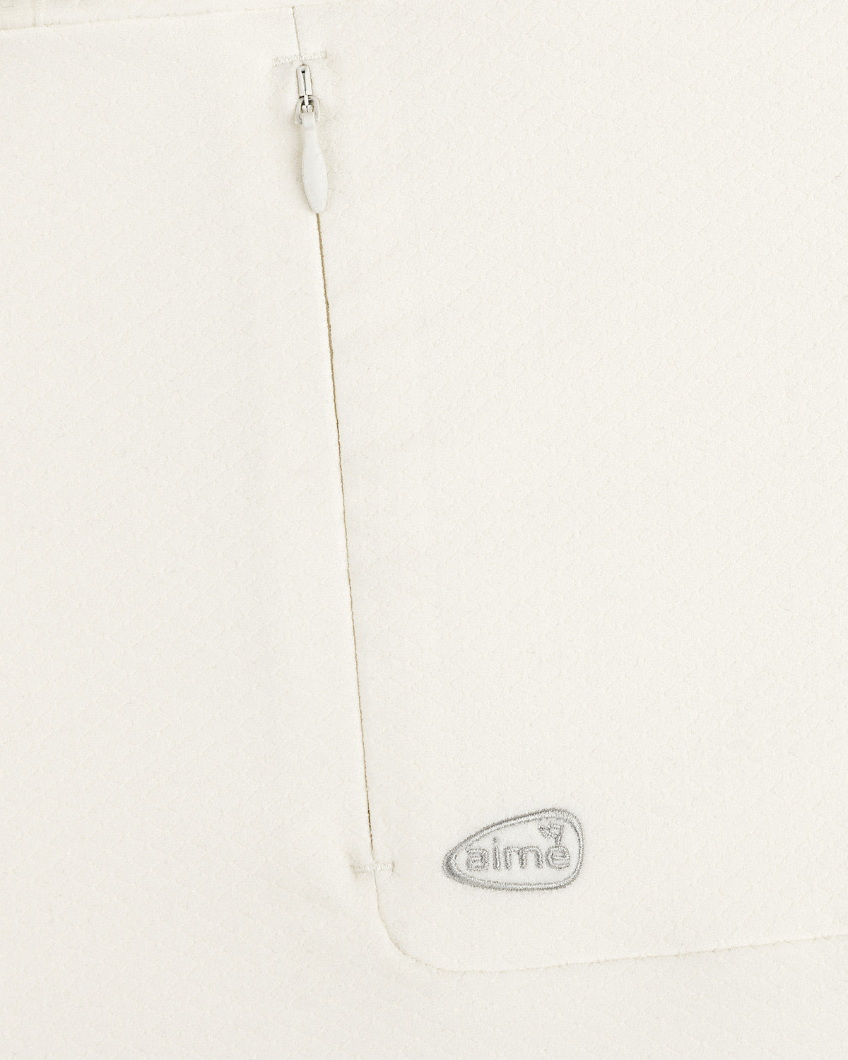 Close-up of ALD Golf Quarter Zip Pullover in white with textured fabric, zipper, and gray embroidered aimé logo.
