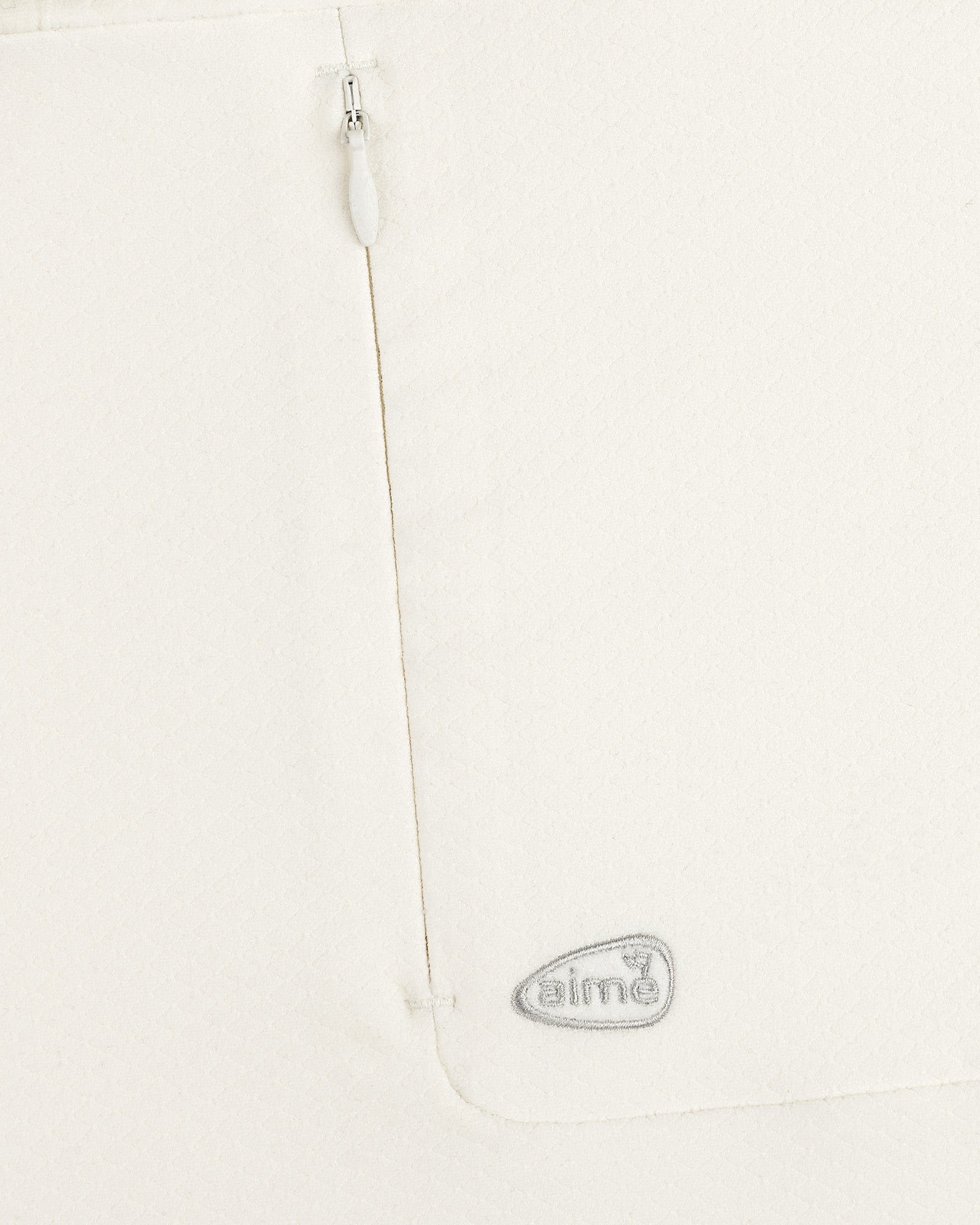 Close-up of ALD Golf Quarter Zip Pullover in white with textured fabric, zipper, and gray embroidered aimé logo.
