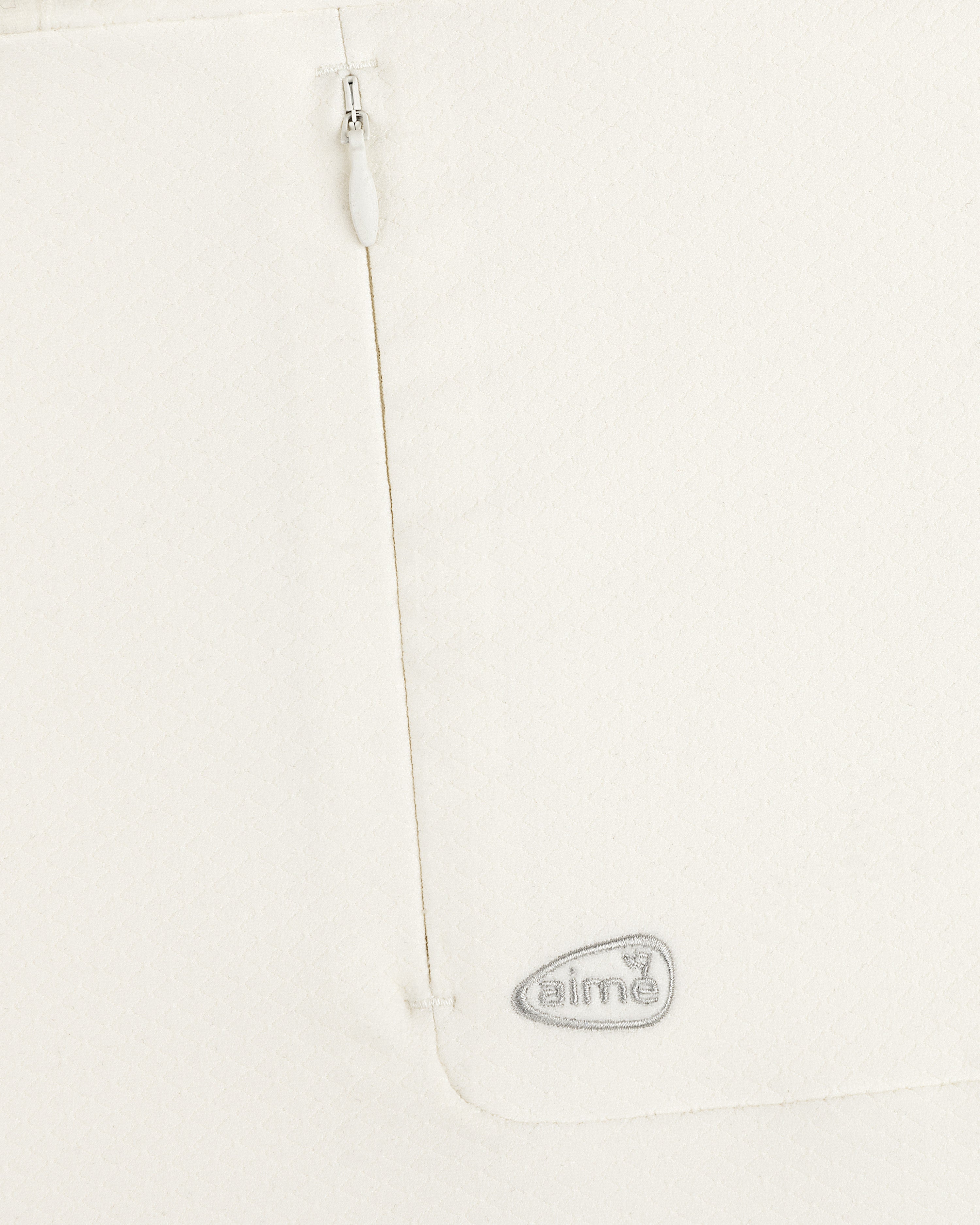 Close-up of ALD Golf Quarter Zip Pullover in white with textured fabric, zipper, and gray embroidered aimé logo.