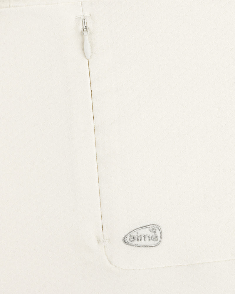 Close-up of ALD Golf Quarter Zip Pullover in white with textured fabric, zipper, and gray embroidered aimé logo.