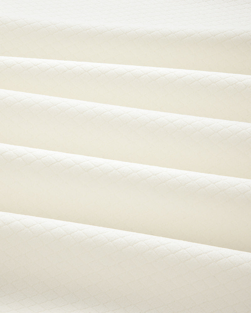 Close-up of folded ALD Golf Quarter Zip Pullover in cream with a subtle diamond pattern and soft shadows.