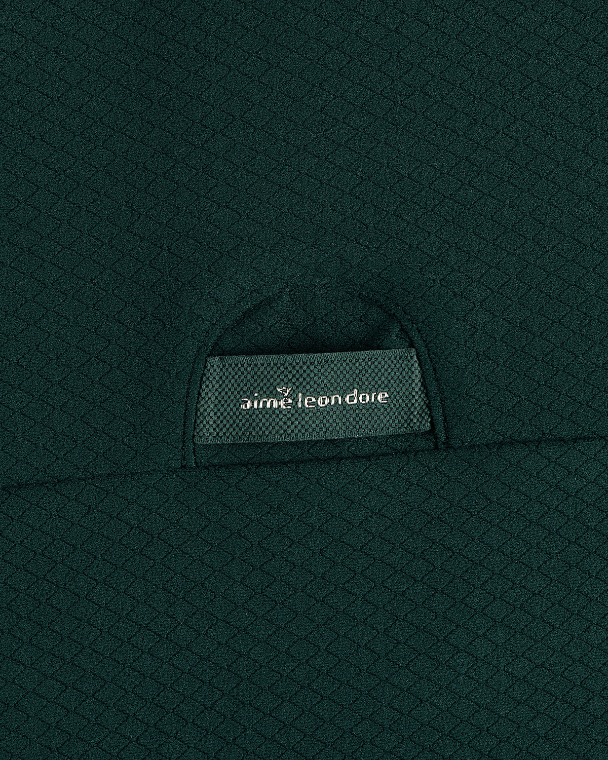 Close-up of green textured fabric on the ALD Golf Quarter Zip Pullover with an aime leon dore label on a small pocket.