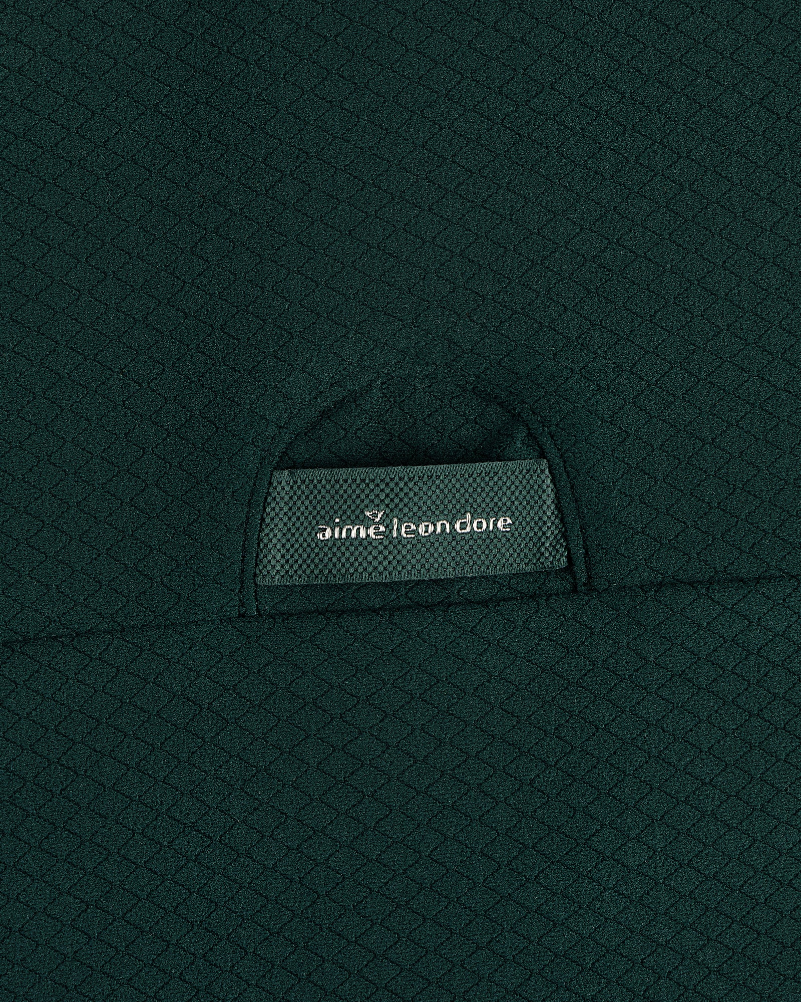 Close-up of green textured fabric on the ALD Golf Quarter Zip Pullover with an aime leon dore label on a small pocket.