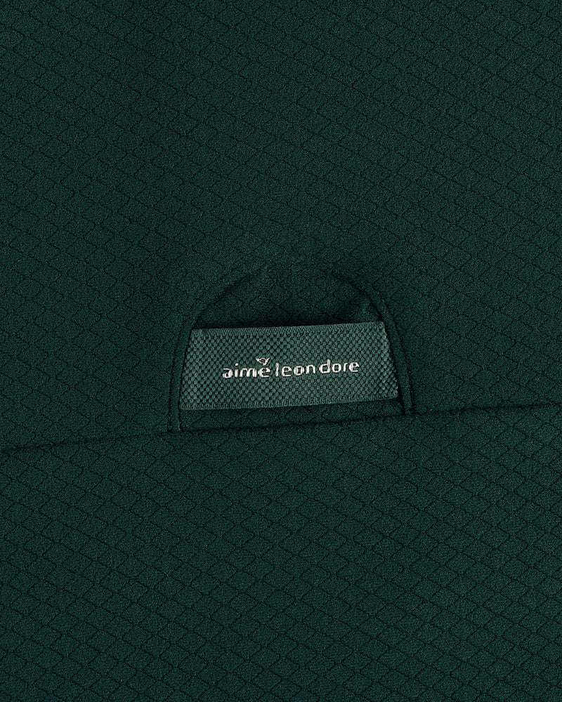 Close-up of green textured fabric on the ALD Golf Quarter Zip Pullover with an aime leon dore label on a small pocket.