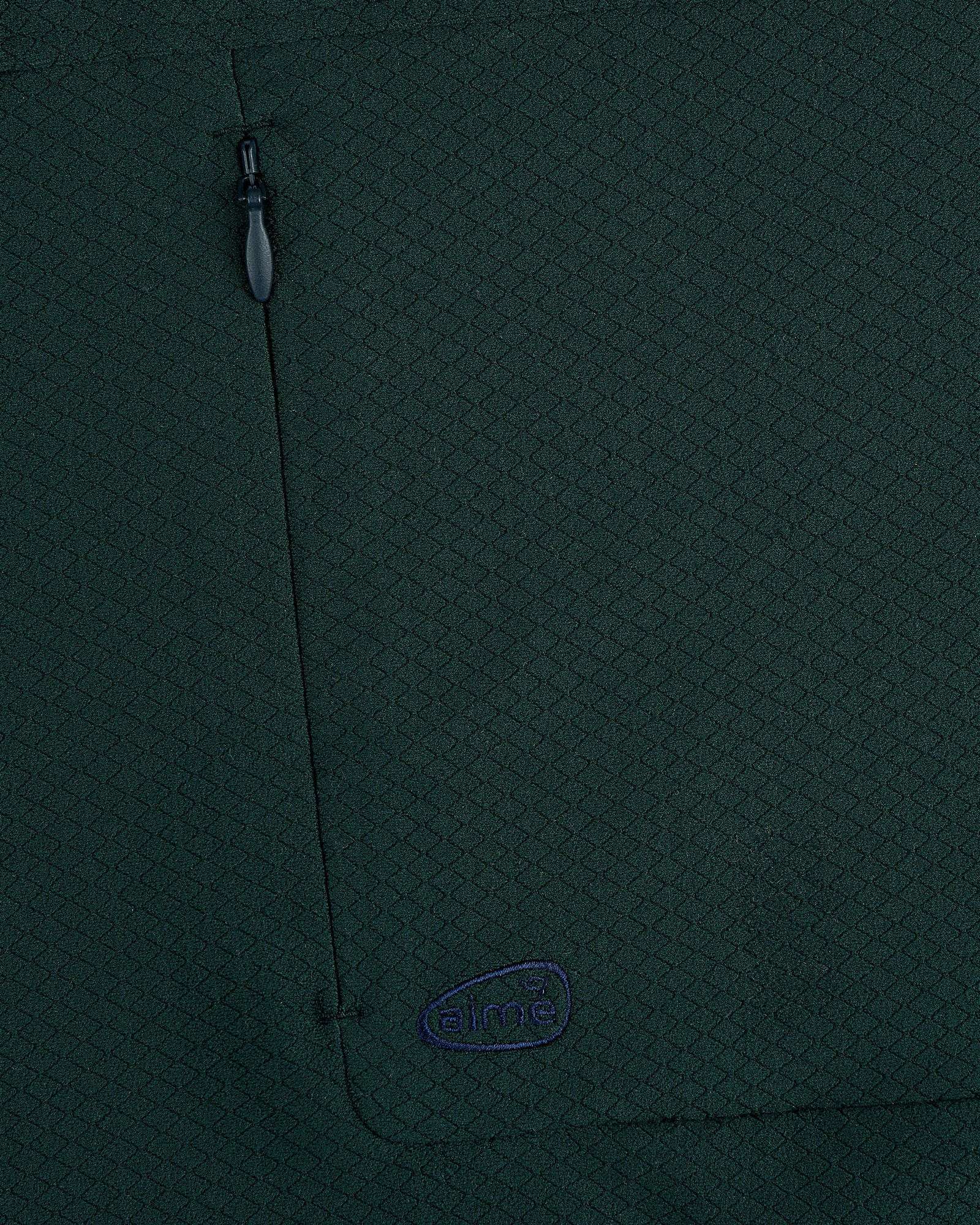 Close-up of dark green ALD Golf Quarter Zip Pullover with zipper pocket and small blue aimé embroidered logo.