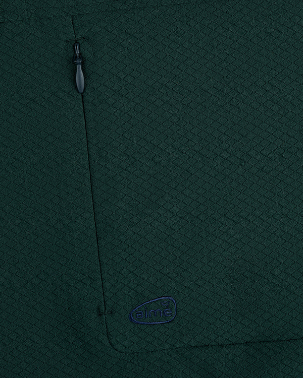 Close-up of dark green ALD Golf Quarter Zip Pullover with zipper pocket and small blue aimé embroidered logo.