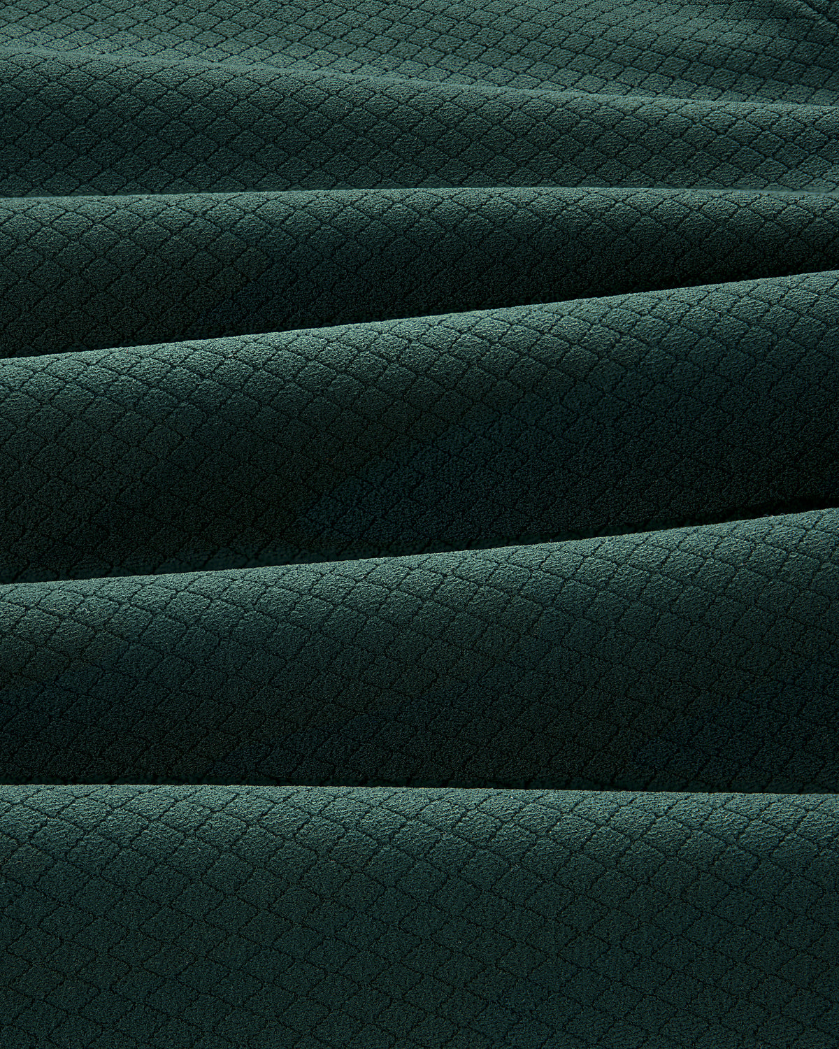 Close-up of folded ALD Golf Quarter Zip Pullover in dark green with a small diamond pattern texture.