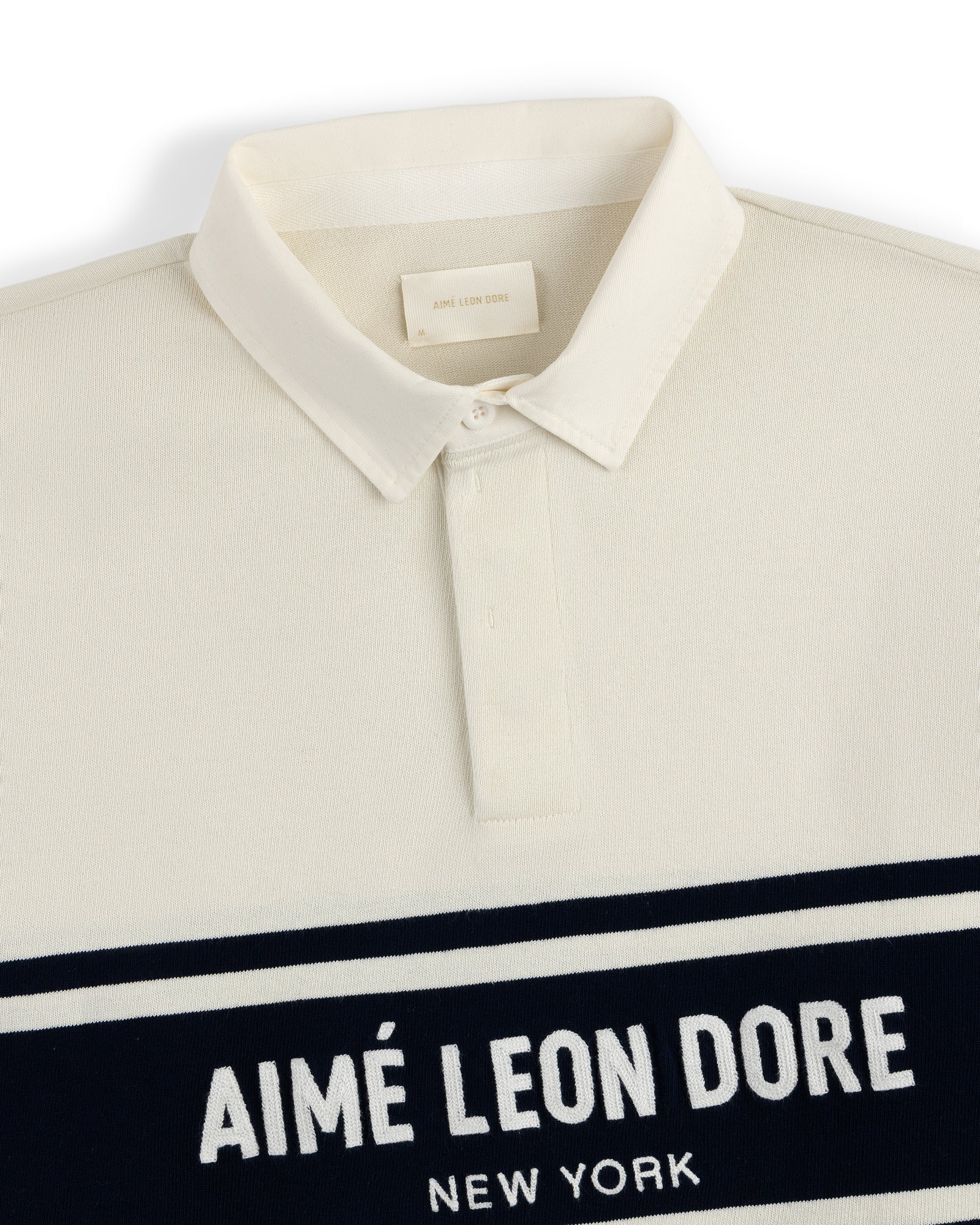 Cream-colored Chest Stripe Logo Rugby with AIMÉ LEON DORE NEW YORK in white on a navy chest stripe.