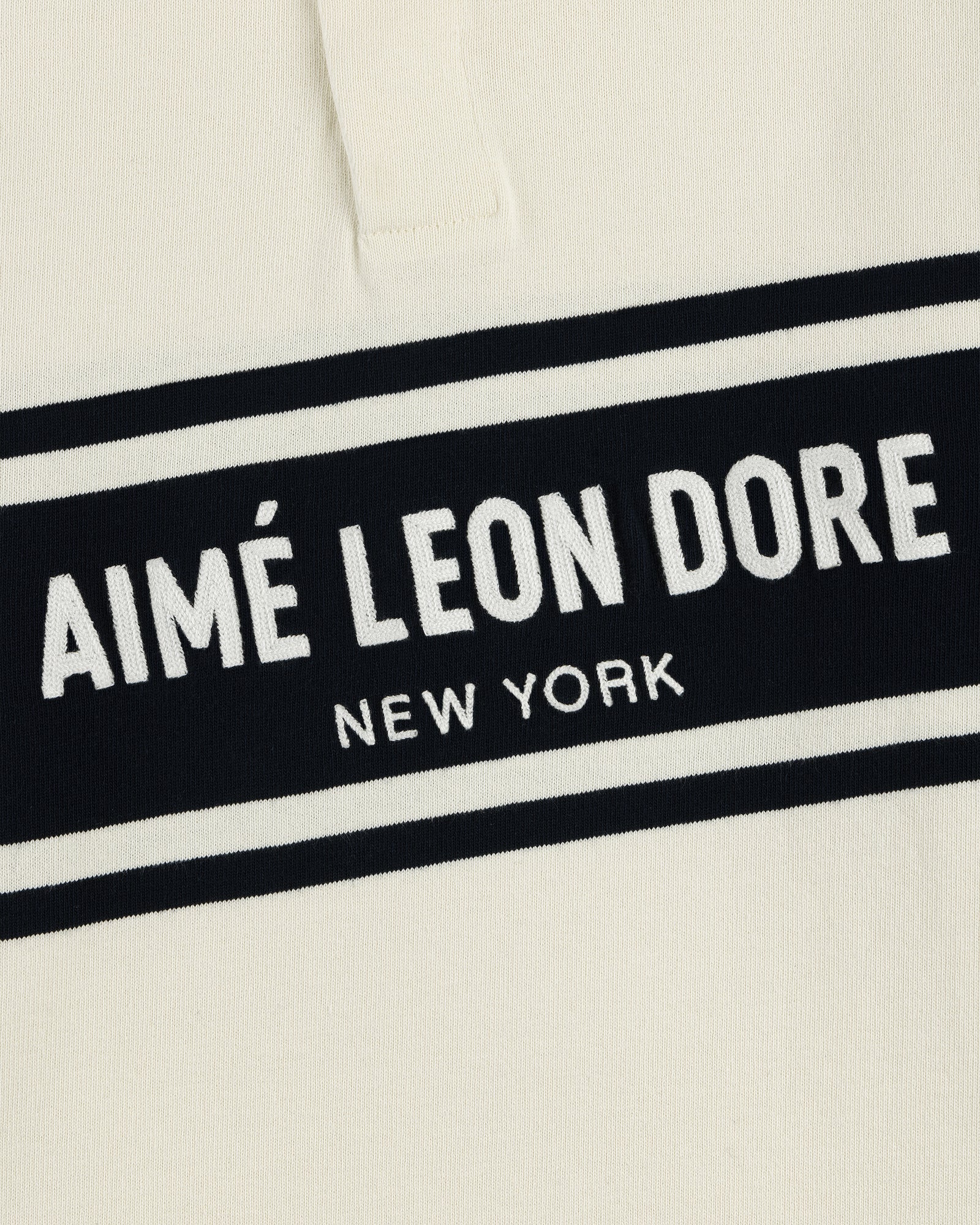 Cream-colored Chest Stripe Logo Rugby with AIMÉ LEON DORE NEW YORK embroidered in white on a black rectangle.