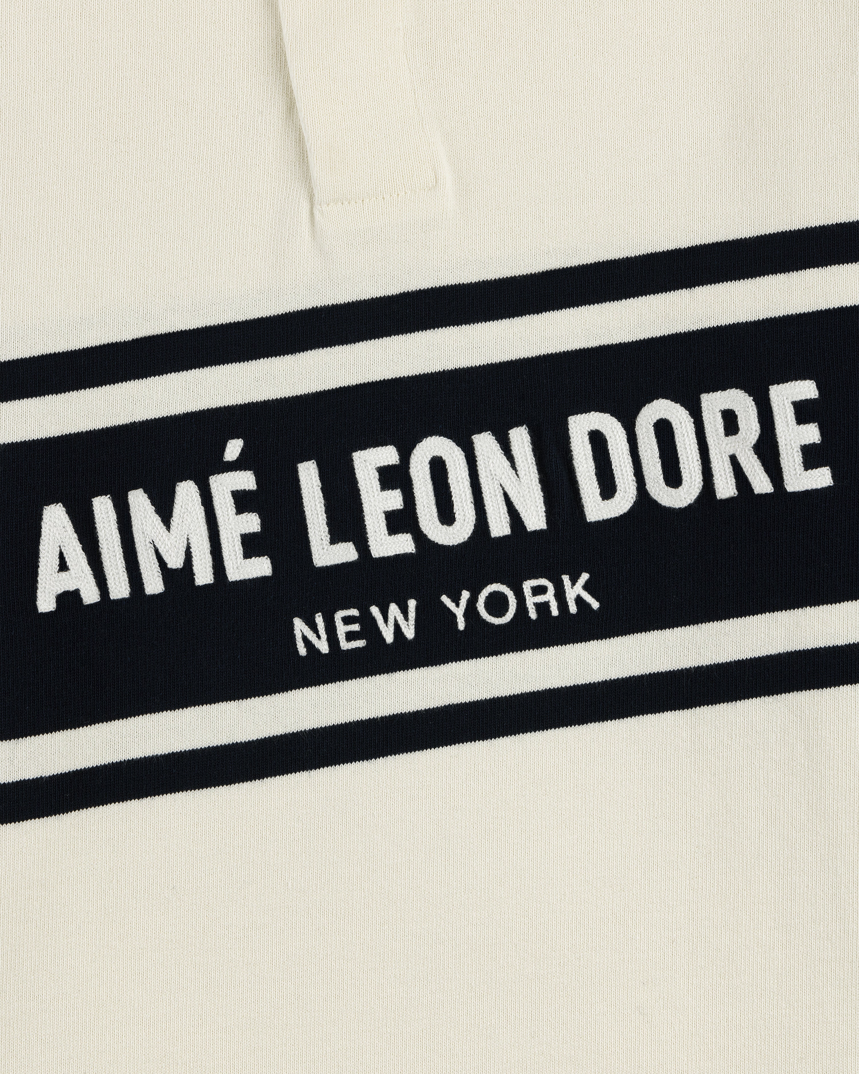 Cream-colored Chest Stripe Logo Rugby with AIMÉ LEON DORE NEW YORK embroidered in white on a black rectangle.