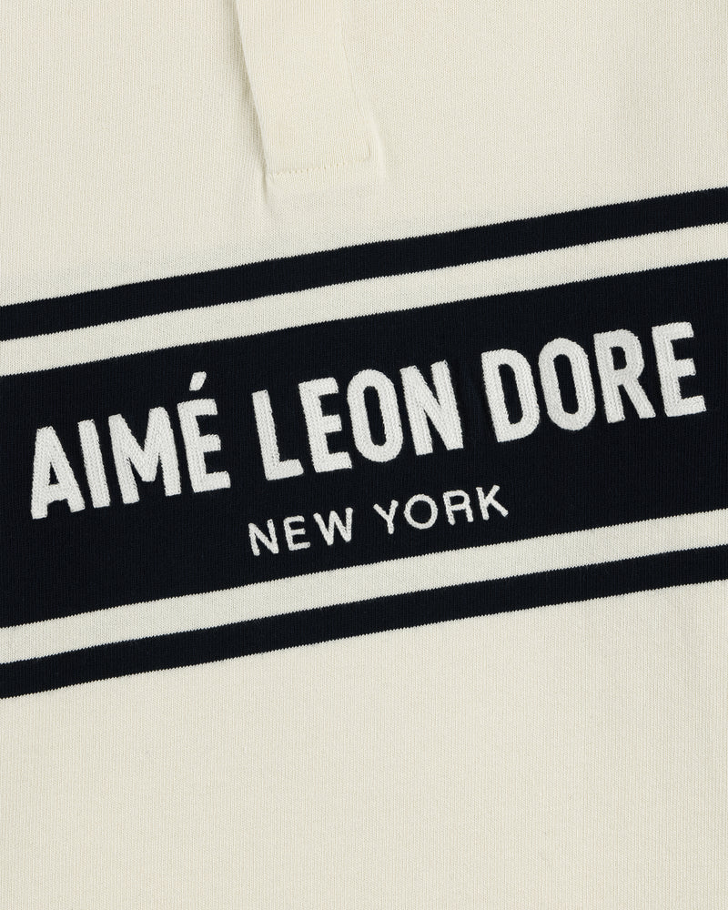 Cream-colored Chest Stripe Logo Rugby with AIMÉ LEON DORE NEW YORK embroidered in white on a black rectangle.