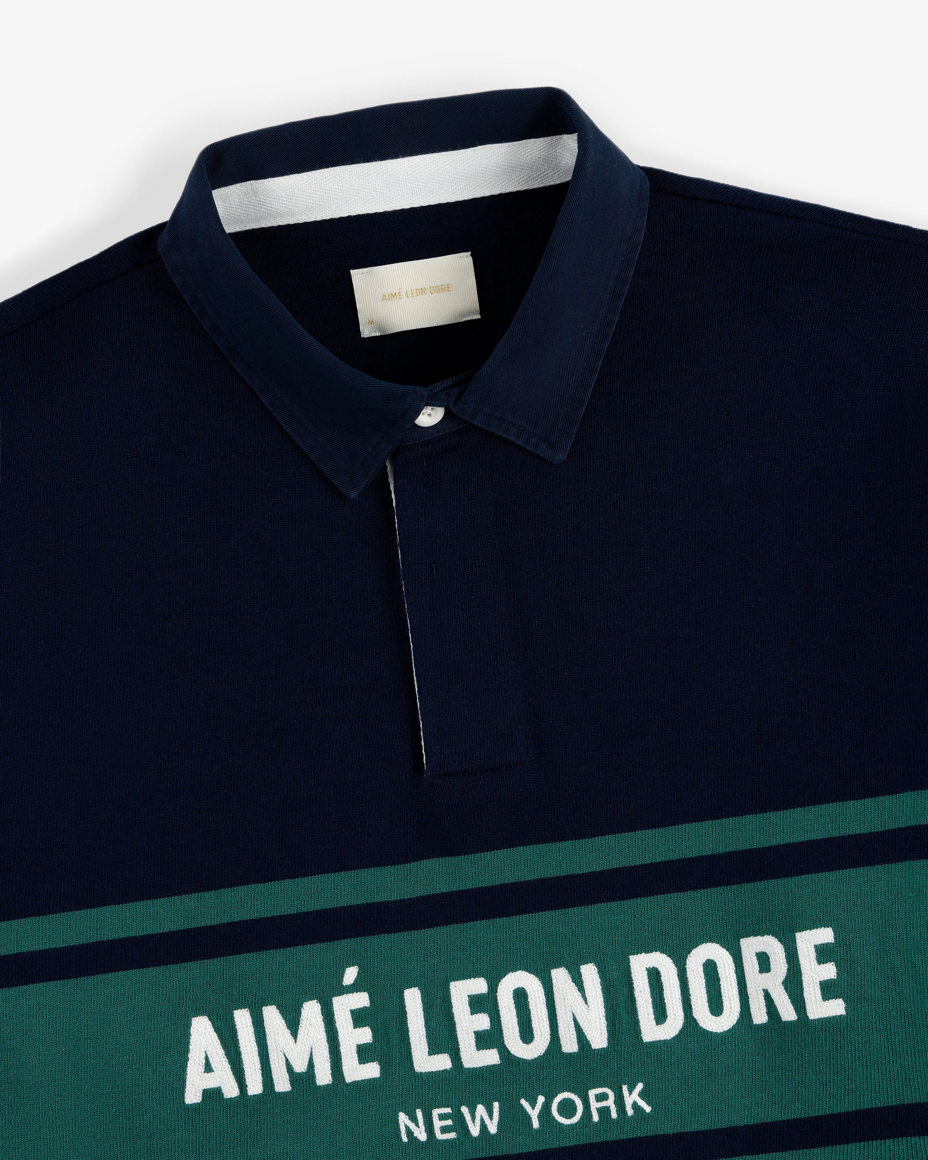 Navy Chest Stripe Logo Rugby with collar and "AIMÉ LEON DORE NEW YORK" in white on a green chest stripe.