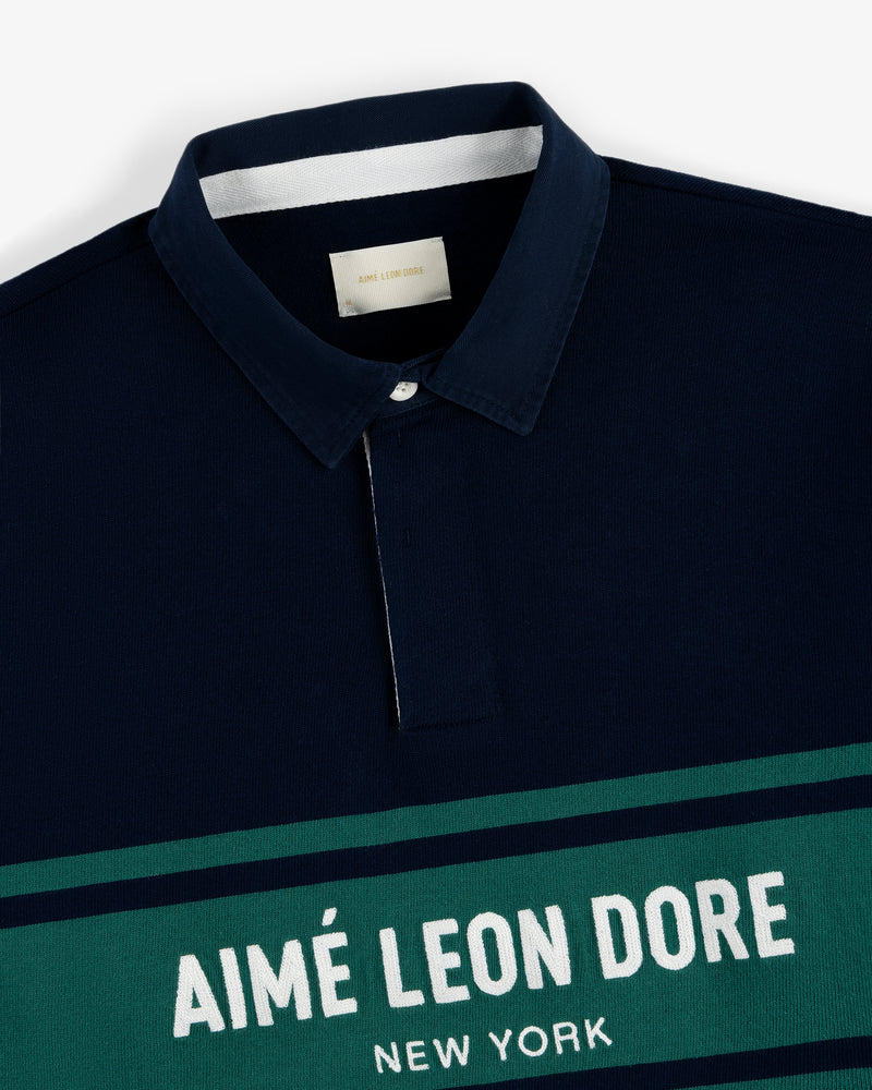 Navy Chest Stripe Logo Rugby with collar and "AIMÉ LEON DORE NEW YORK" in white on a green chest stripe.
