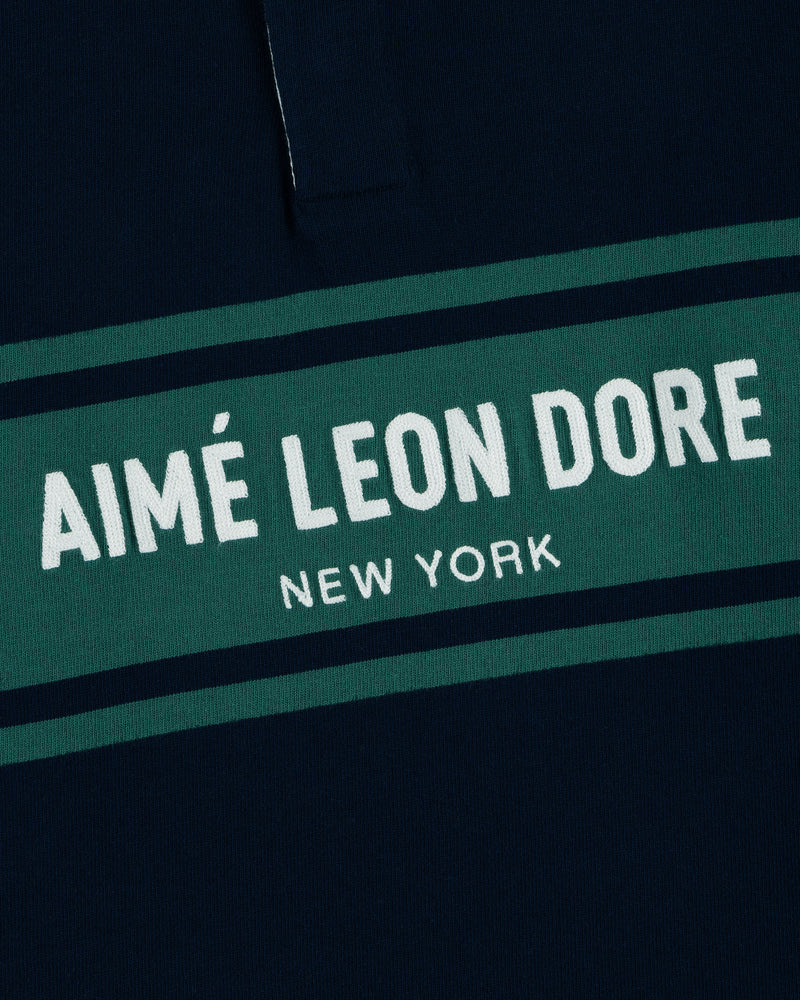Close-up of the Chest Stripe Logo Rugby with AIMÉ LEON DORE NEW YORK printed on green and navy blue fabric.