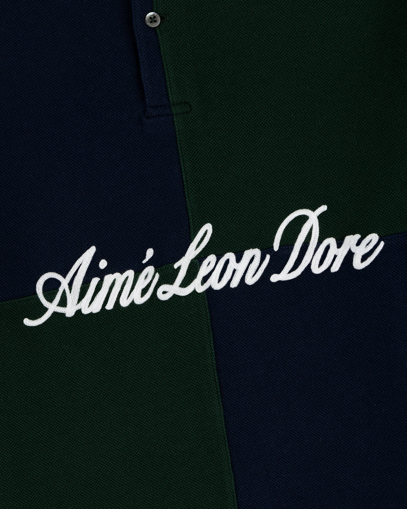 Close-up of a Color Blocked Pique Polo with Aimé Leon Dore embroidered in white cursive on green and navy blocks.