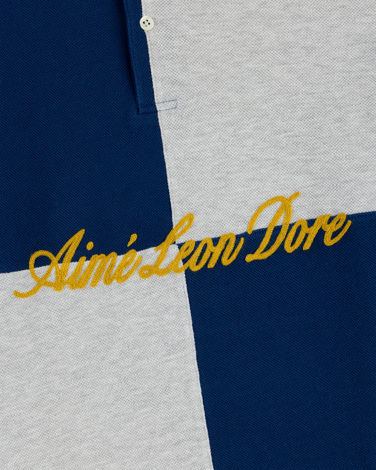 Close-up of the Color Blocked Pique Polo’s blue and gray checkered fabric with yellow Aimé Leon Dore embroidery.