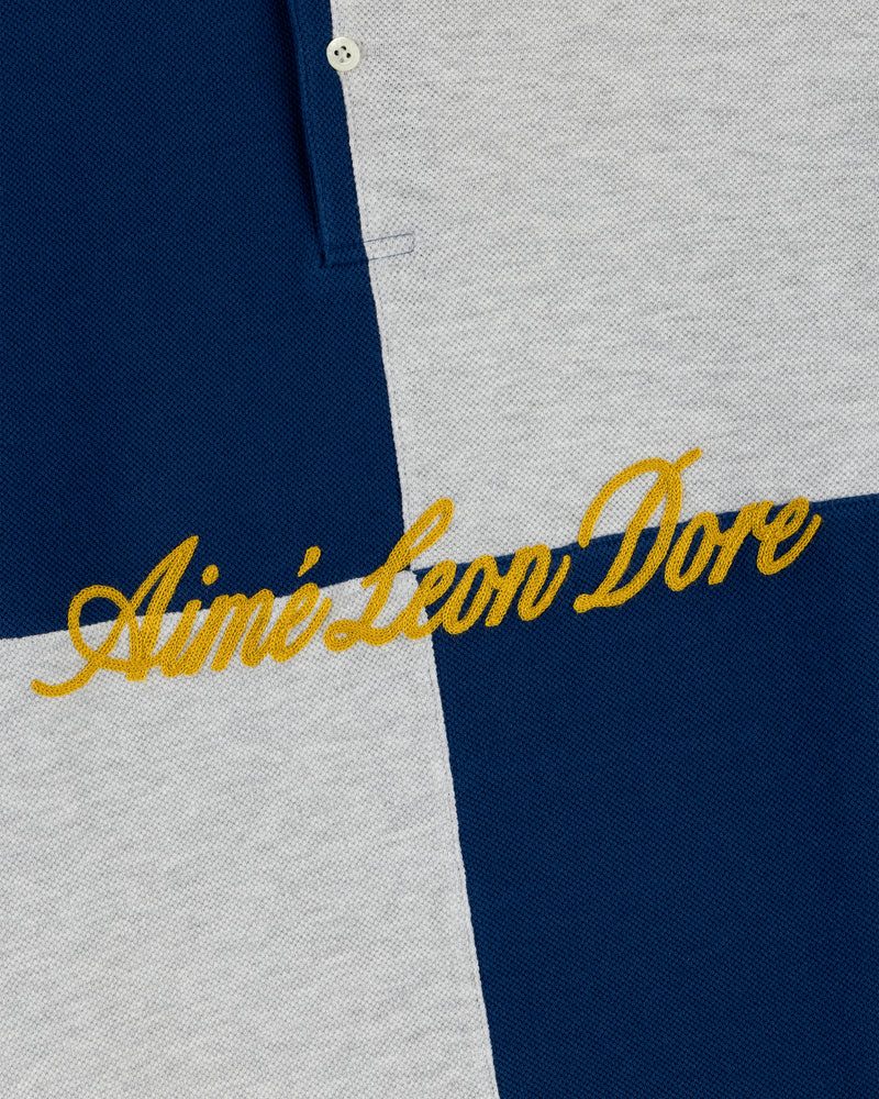 Close-up of the Color Blocked Pique Polo’s blue and gray checkered fabric with yellow Aimé Leon Dore embroidery.