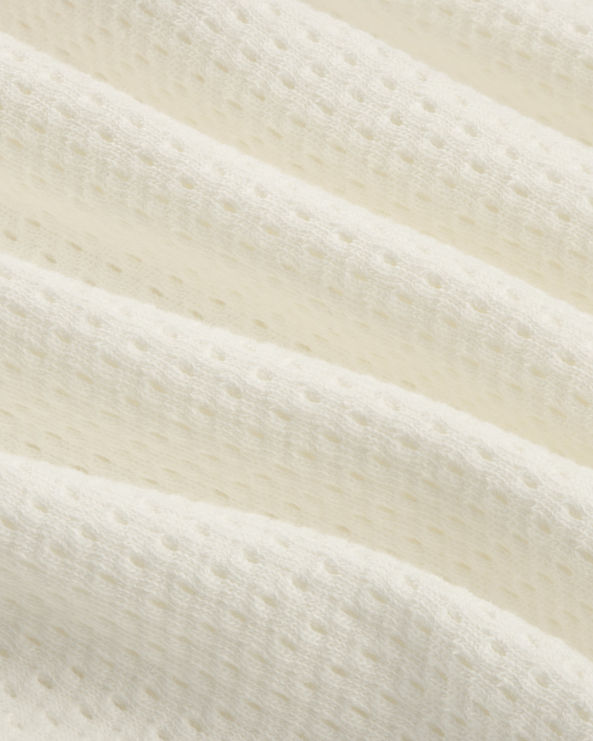 Close-up of the Pointelle Stacked Logo Tee's soft, white textured fabric with small perforations and wavy folds.