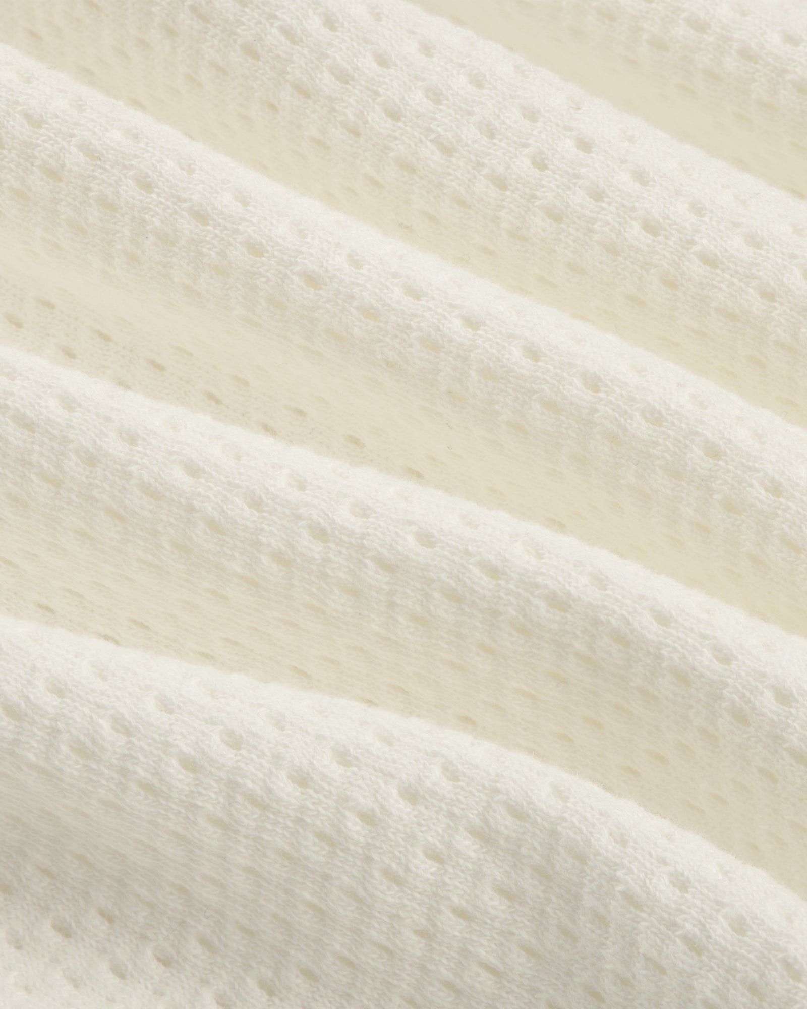 Close-up of the Pointelle Stacked Logo Tee's soft, white textured fabric with small perforations and wavy folds.
