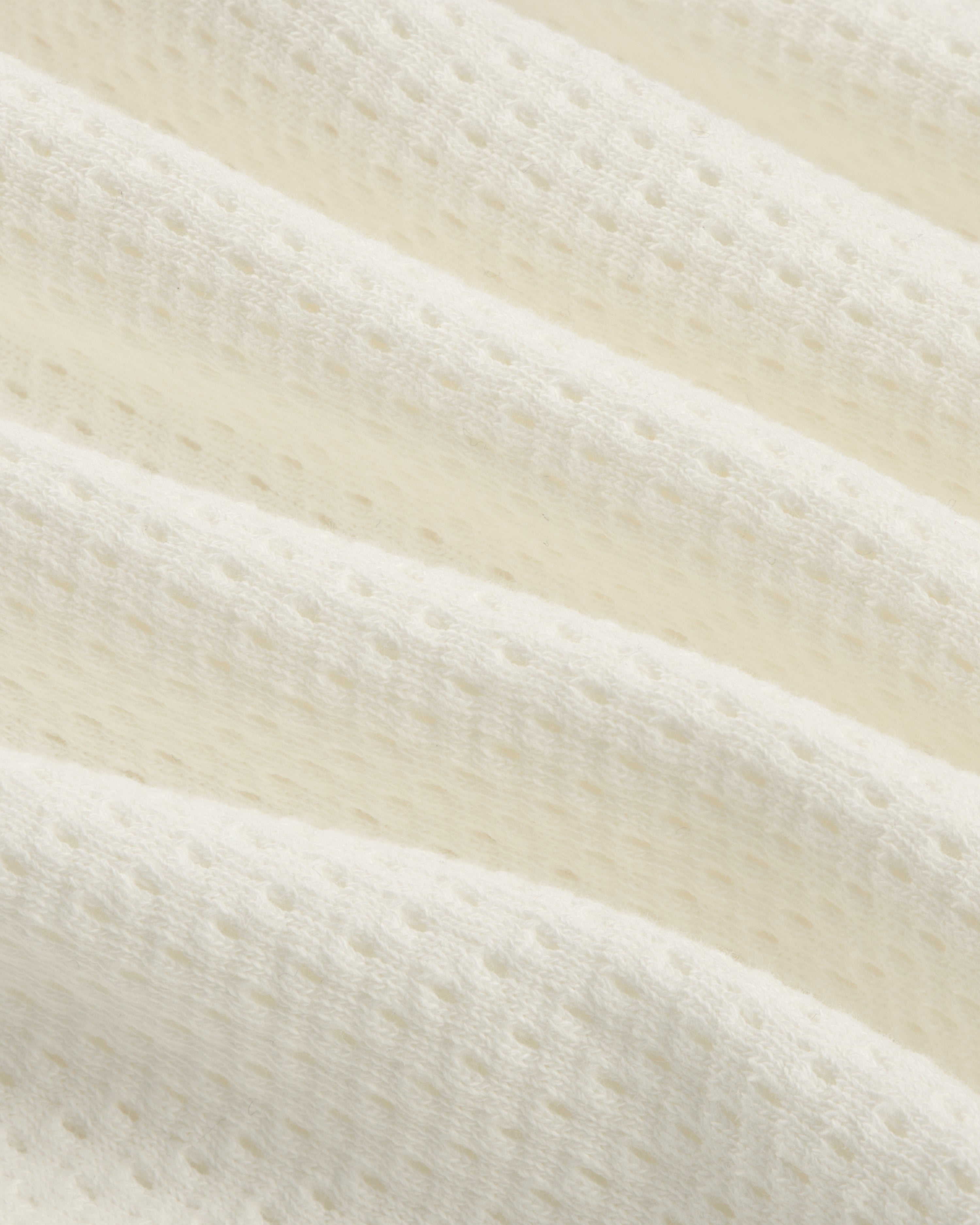 Close-up of the Pointelle Stacked Logo Tee's soft, white textured fabric with small perforations and wavy folds.