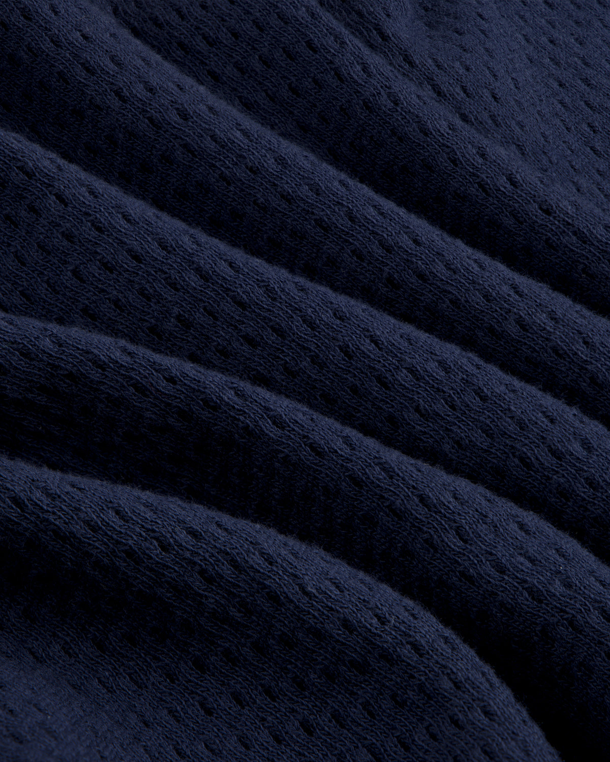 Close-up of the Pointelle Stacked Logo Tee in dark blue, featuring ribbed texture, perforations, and soft fabric folds.