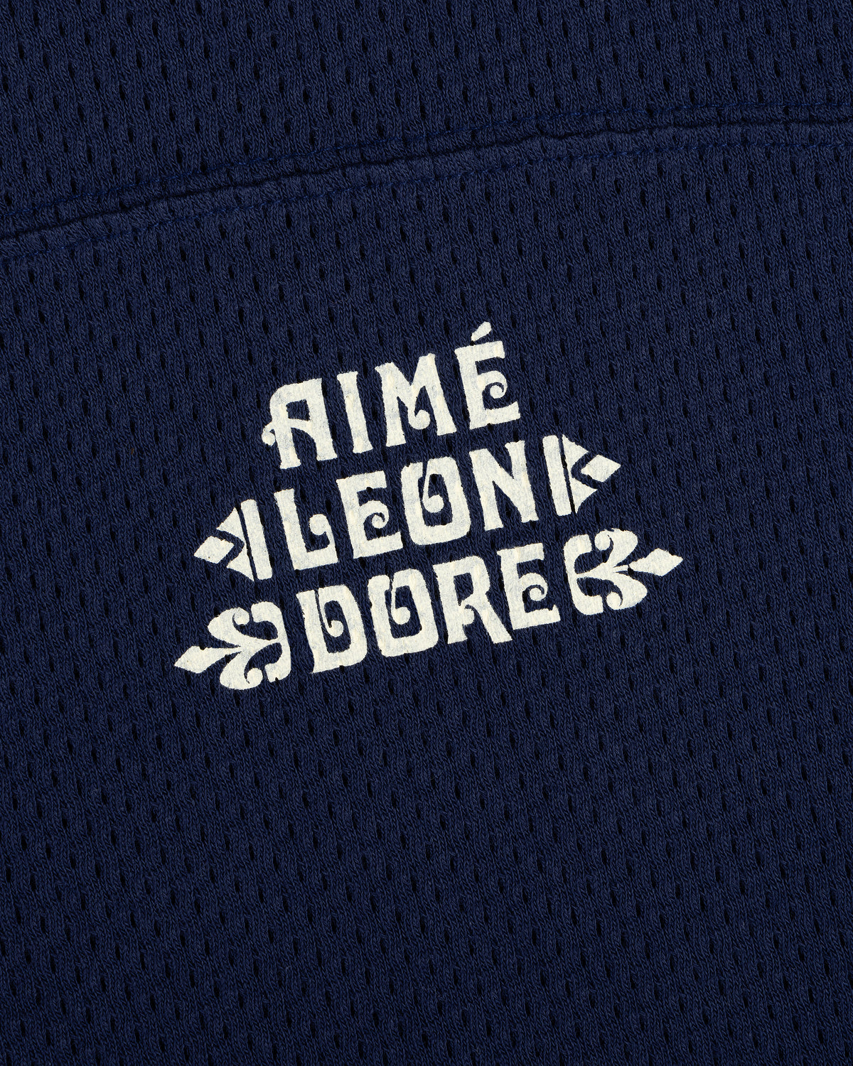 Close-up of white Pointelle Stacked Logo Tee text on navy blue mesh fabric.