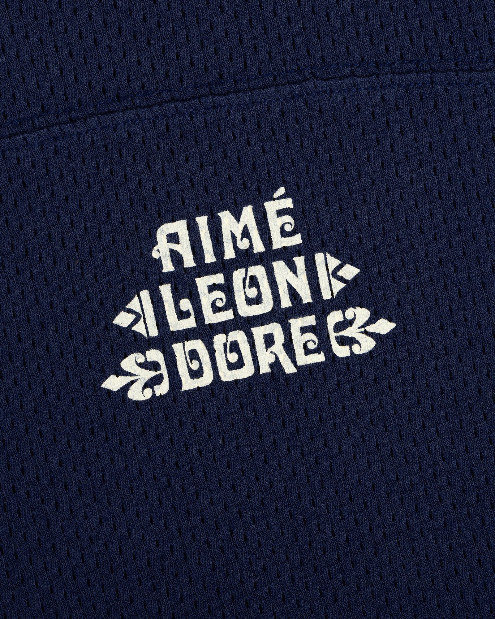 Close-up of white Pointelle Stacked Logo Tee text on navy blue mesh fabric.