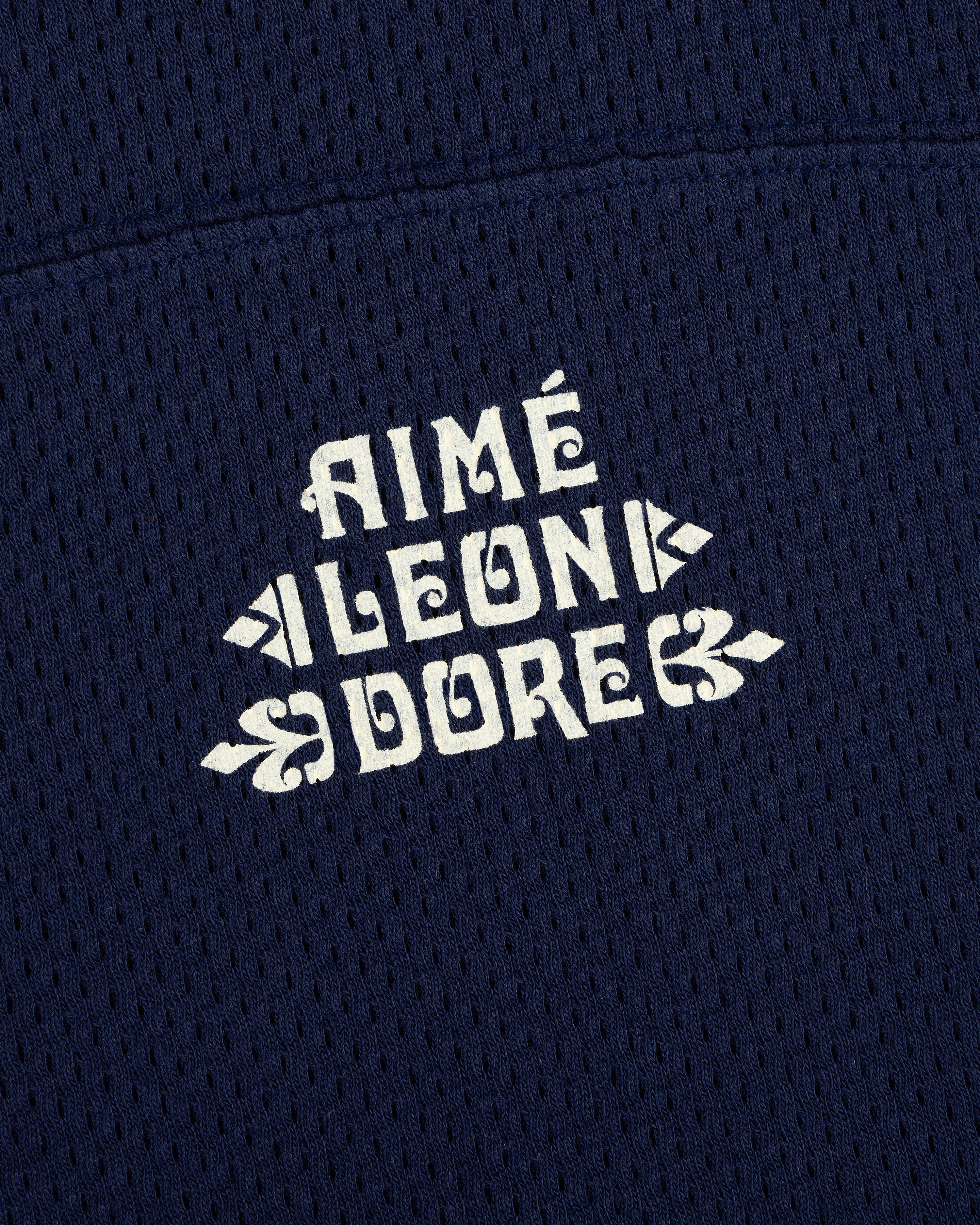 Close-up of white Pointelle Stacked Logo Tee text on navy blue mesh fabric.
