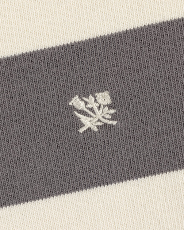 Close-up of the Striped Crest Rugby showing gray and white stripes with a small white floral embroidery at the center.