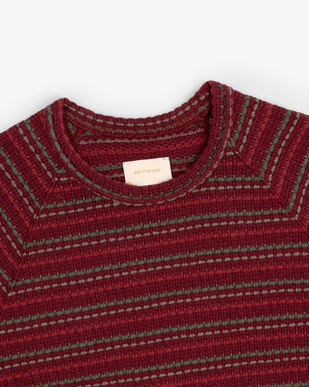 Close-up of a ribbed maroon Jacquard Striped Tee with green stripes and a beige collar label.