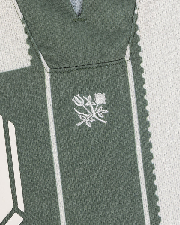Close-up of Aimé Cup Soccer Jersey’s green fabric with white stitching and an embroidered rose and leaf in the center.