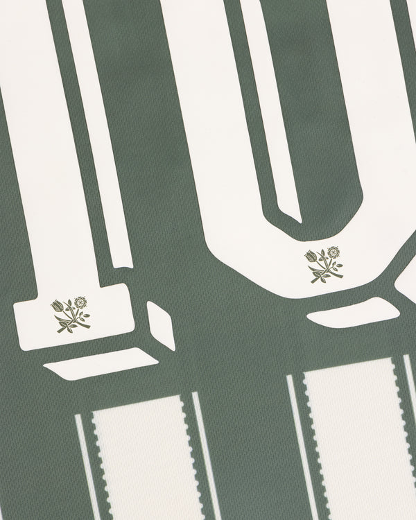Close-up of large white numbers with small flower designs on the green Aimé Cup Soccer Jersey.