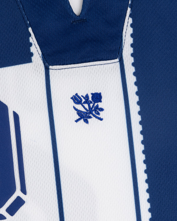 Close-up of the Aimé Cup Soccer Jersey in blue and white with a small blue rose emblem stitched on the chest.