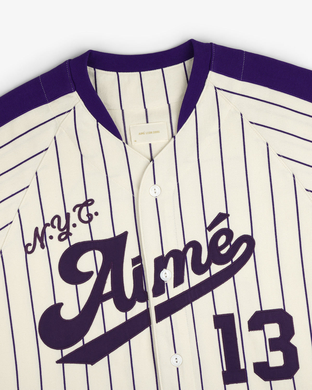Aimé Baseball Jersey in cream and purple pinstripes with M.Y.C. Aimé and number 13 on the front.