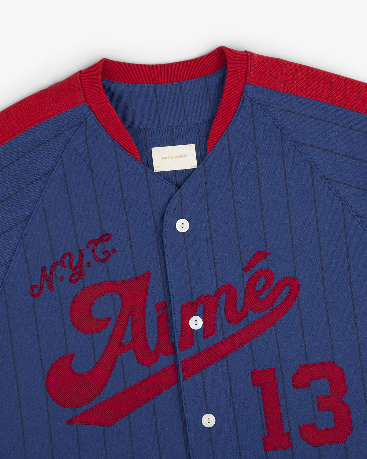 Aimé Baseball Jersey: Blue pinstripes, red N.Y.C. Aimé lettering, red collar/shoulders, and number 13.
