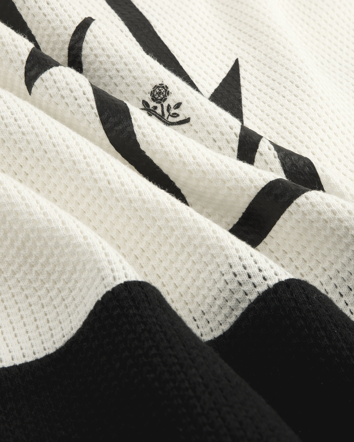 Close-up of the Long-Sleeve Mesh Enduro Tee featuring white mesh with black abstract shapes and a small floral emblem.