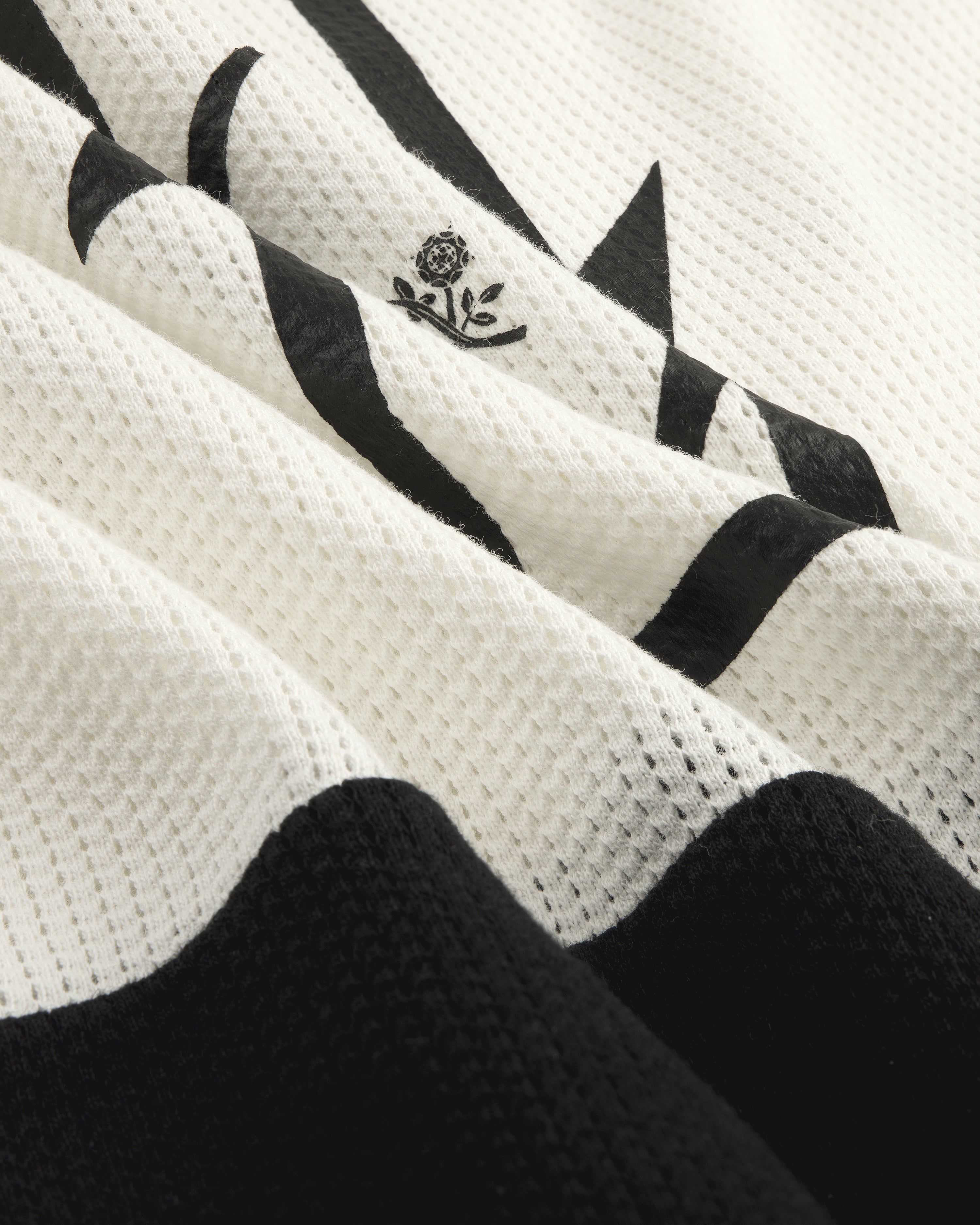 Close-up of the Long-Sleeve Mesh Enduro Tee featuring white mesh with black abstract shapes and a small floral emblem.