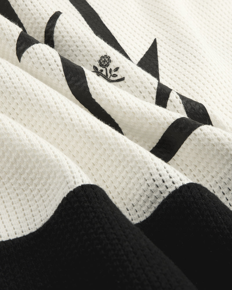 Close-up of the Long-Sleeve Mesh Enduro Tee featuring white mesh with black abstract shapes and a small floral emblem.