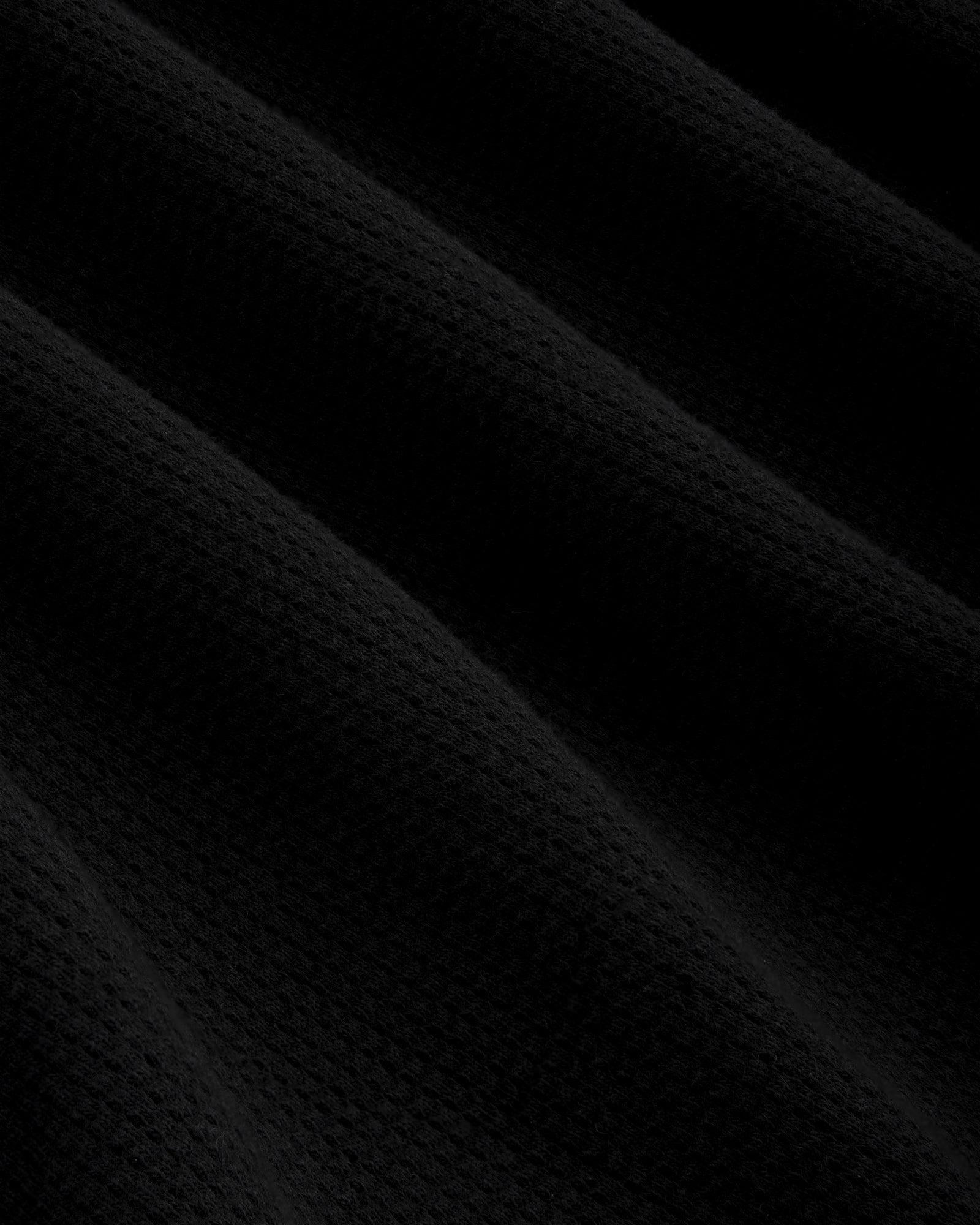 Close-up of Mesh Muscle Tank's black mesh fabric with soft, diagonal folds and gentle, subtle shadows.