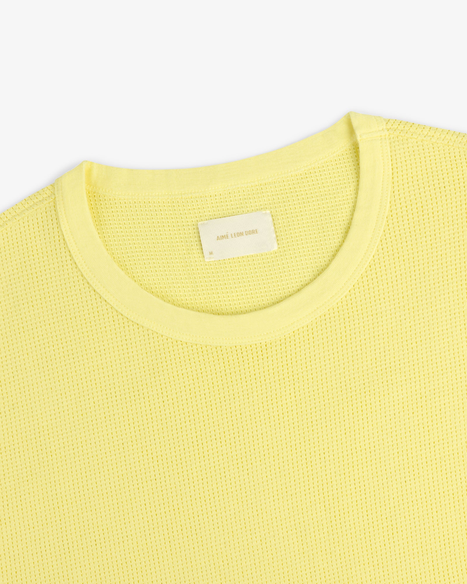 Close-up of a light yellow Mesh Muscle Tank with textured fabric and a visible white tag at the collar.