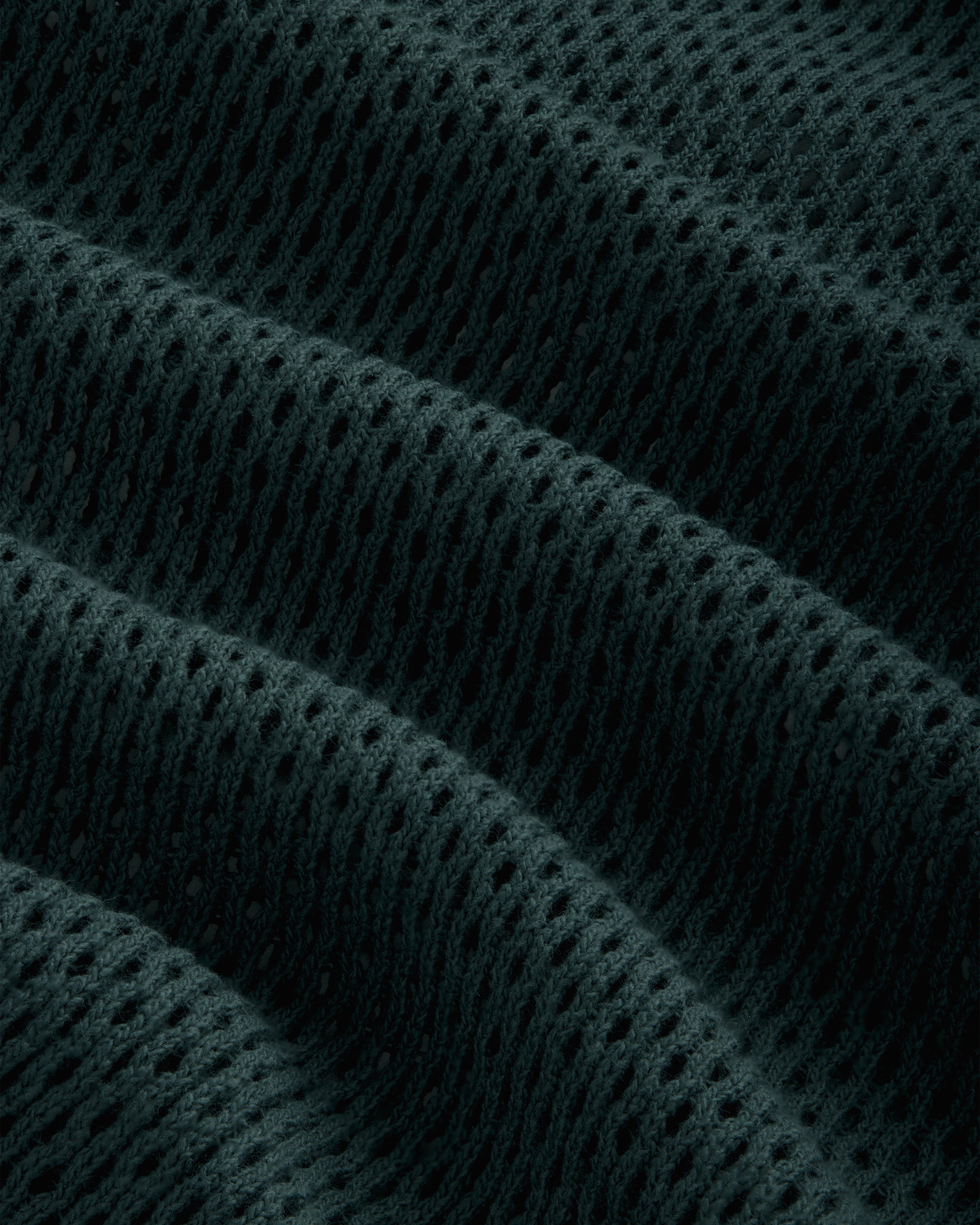 Close-up of Mesh Tank Top fabric, with dark texture and evenly spaced holes creating ridges and waves.