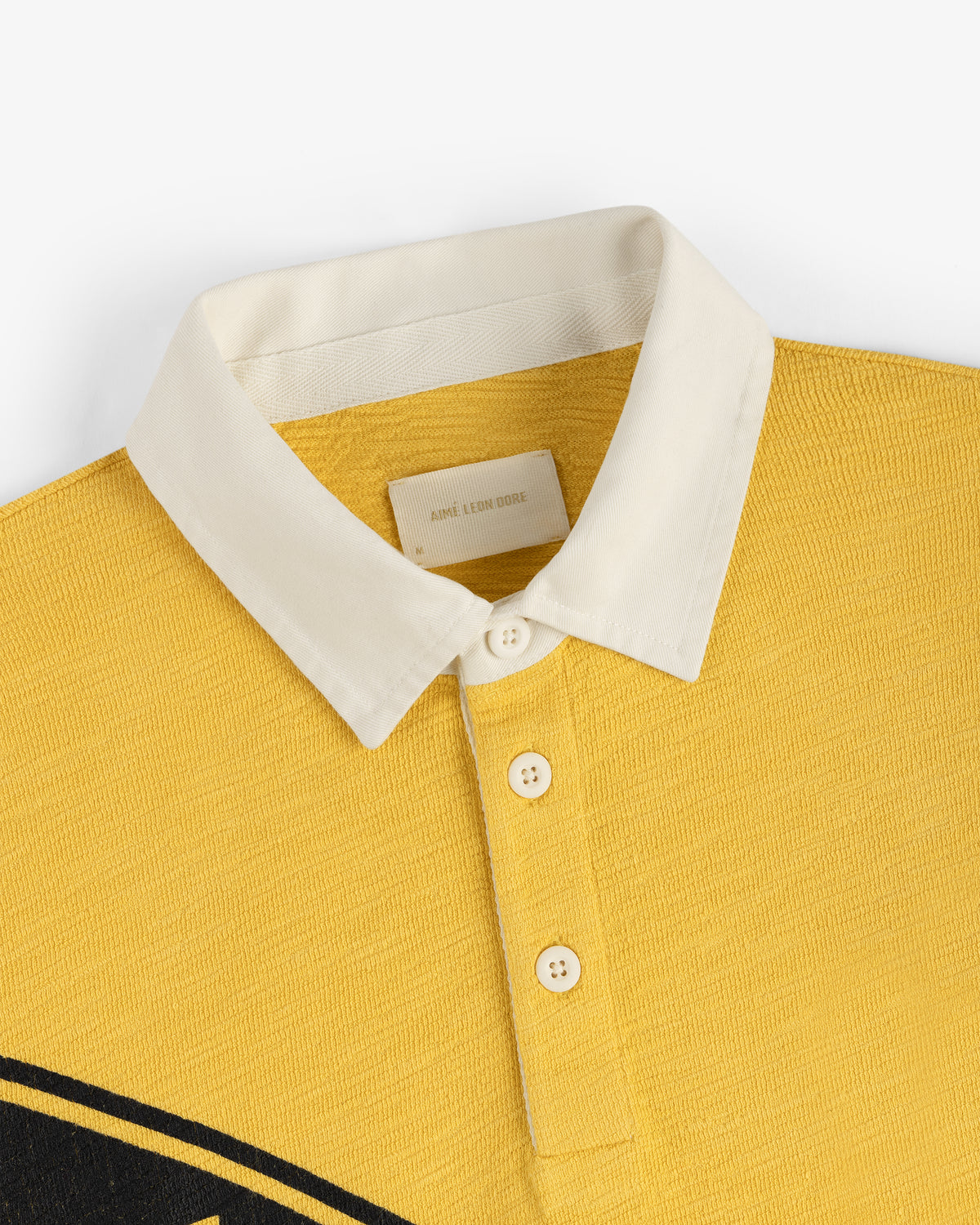 Vintage Slub Rugby: Yellow textured polo with white collar, buttons, black graphic detail, and neutral inside tag.