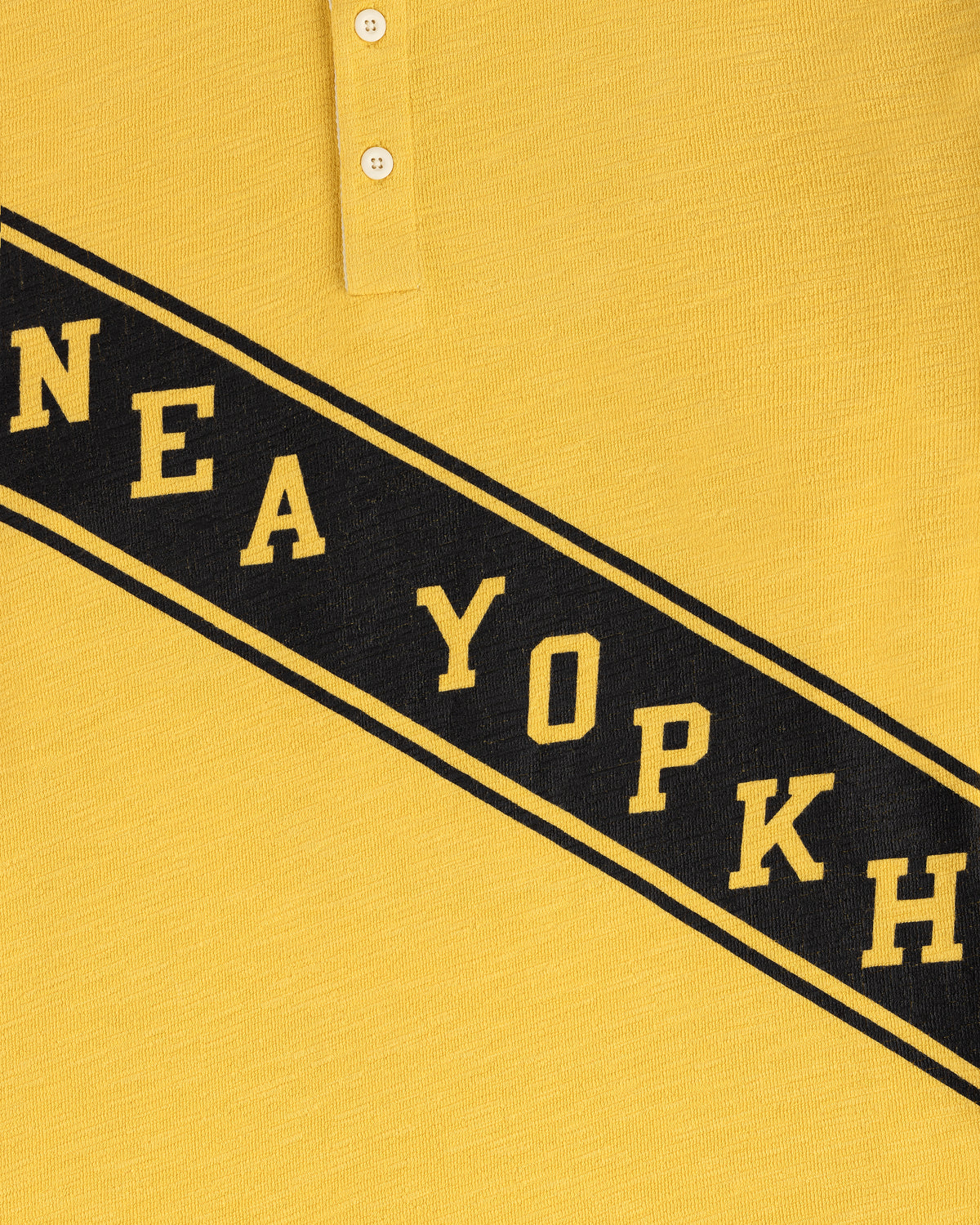 Close-up of the Vintage Slub Rugby in yellow with black diagonal "NEA YOPKH" text and two white top buttons.