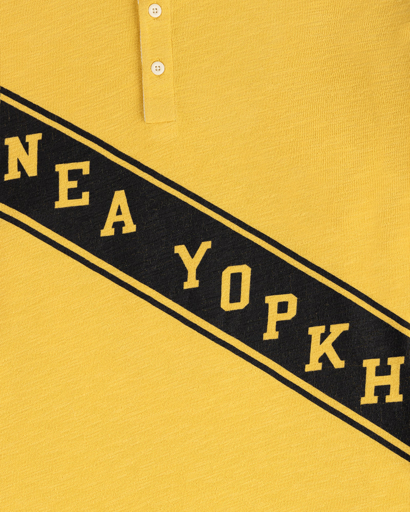 Close-up of the Vintage Slub Rugby in yellow with black diagonal "NEA YOPKH" text and two white top buttons.