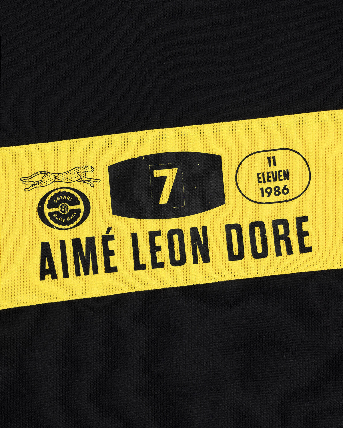 The Long-Sleeve Rally Tee features black fabric with a yellow stripe, AIMÉ LEON DORE, the number 7, and logos.
