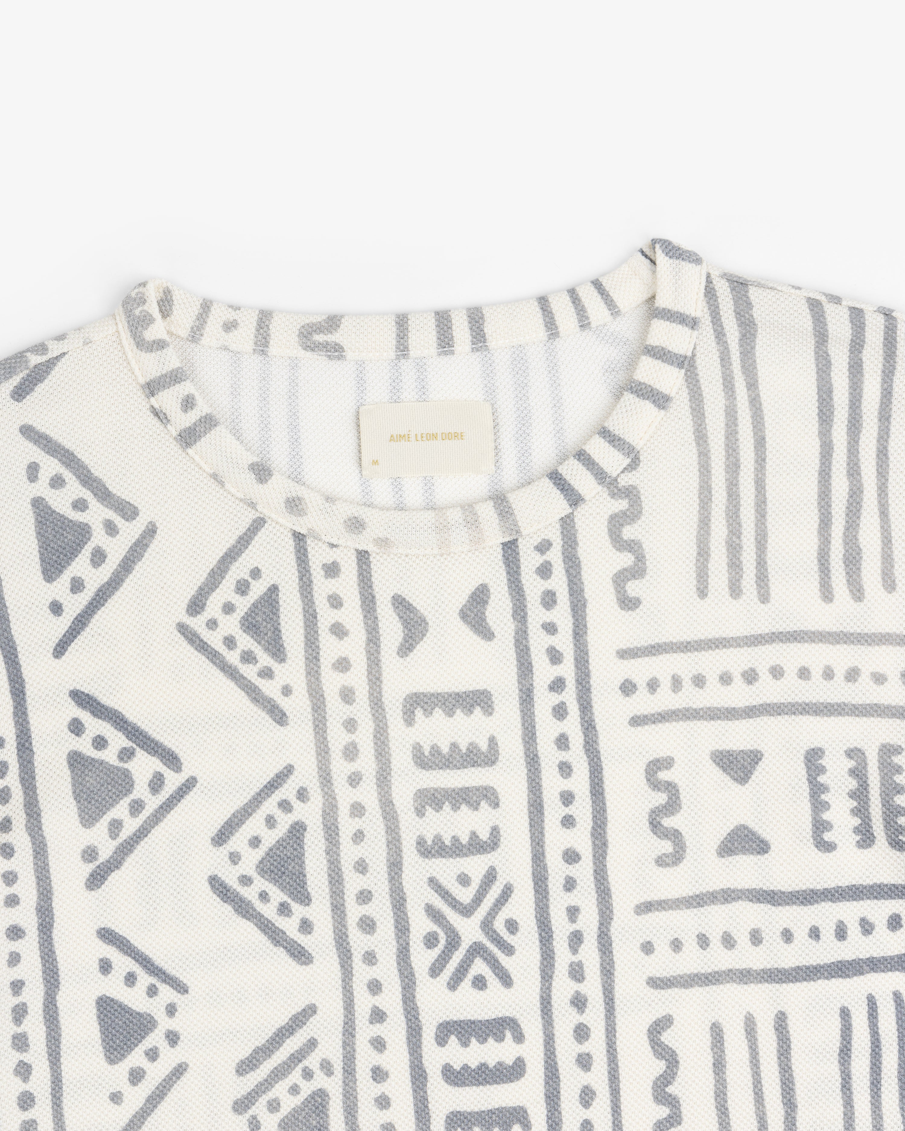 Close-up of the Long-Sleeve Mesh Tapestry Tee featuring gray geometric and tribal-inspired prints on white.