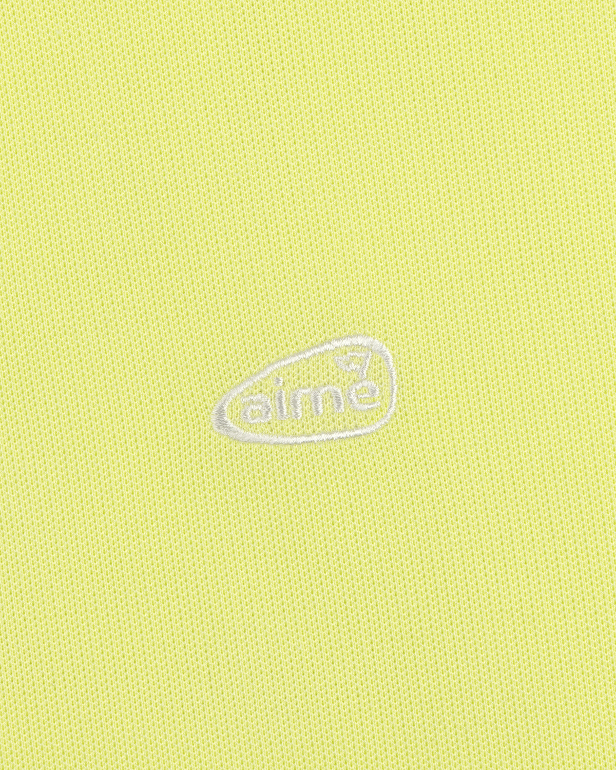 Yellow textured ALD Golf Polo with small white aimé logo inside an irregular oval at the center.