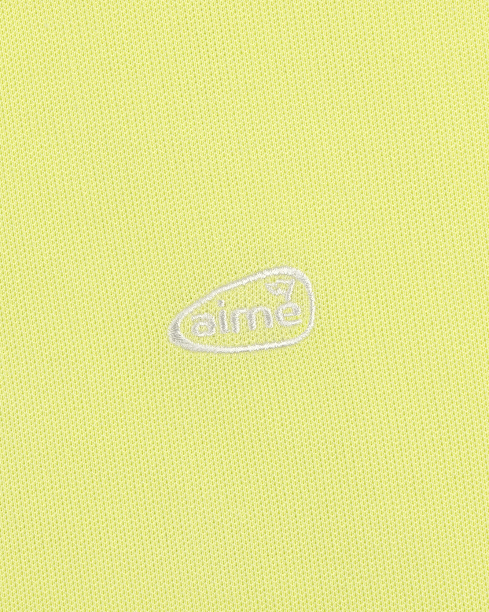 Yellow textured ALD Golf Polo with small white aimé logo inside an irregular oval at the center.