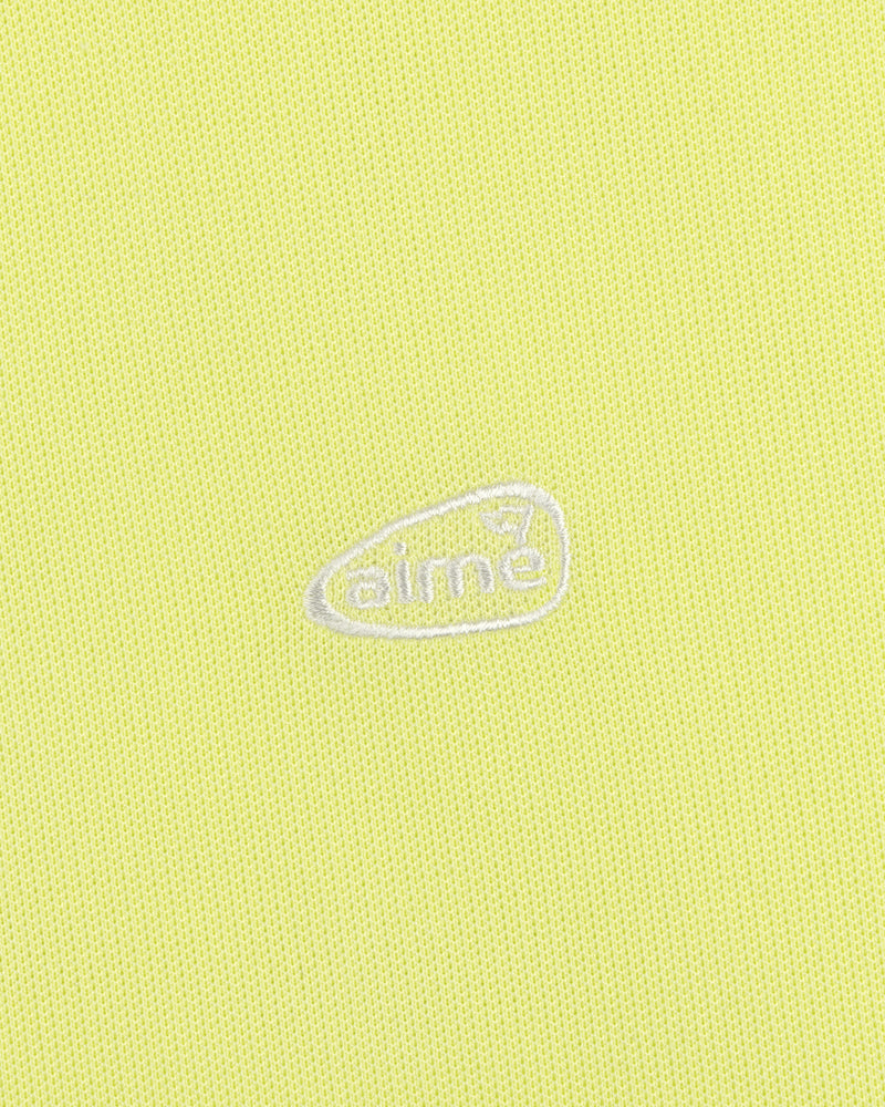 Yellow textured ALD Golf Polo with small white aimé logo inside an irregular oval at the center.